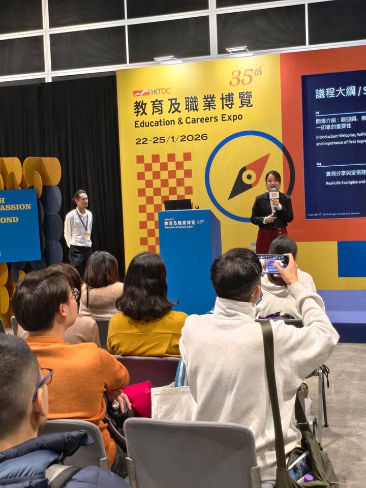 A trainer speaking to an audience on a stage at the "Education & Careers Expo," with attendees listening.