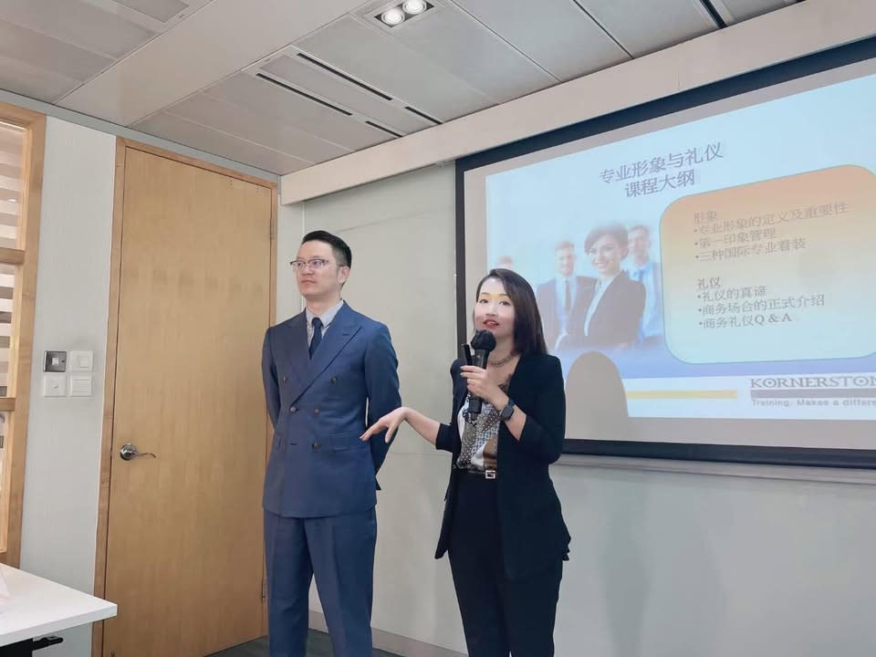Two trainers, a man and a woman, presenting a professional image and etiquette course to an audience.